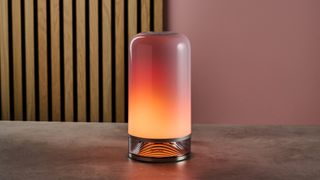 The Govee Table Lamp 2 is lit up in lava-like colors and sits on a stone surface with wooden slats and a pink wall behind.