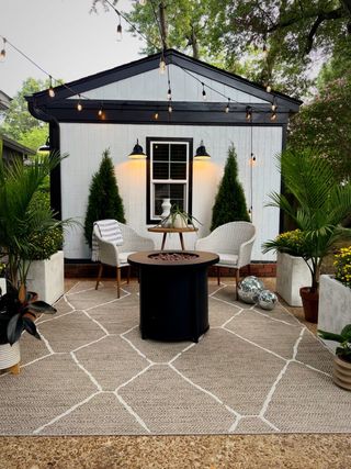 Seasonally decorated yard space with white shed, outdoor rug, chairs and yellow mums