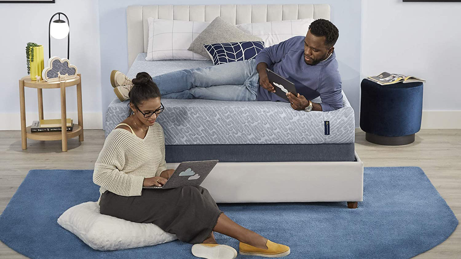 A man lies on the Serta 9 Inch Memory Foam Mattress while a woman sits on the floor working on her laptop