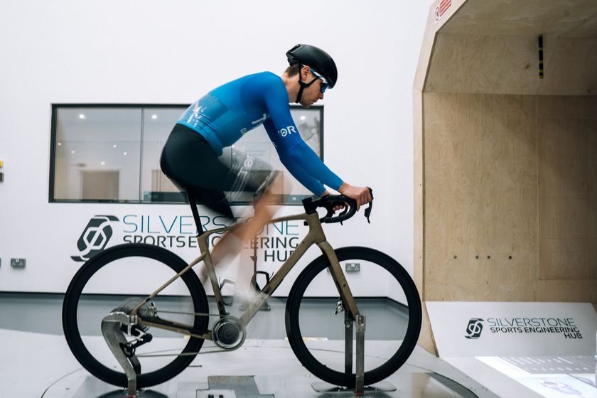 Josh riding in the wind tunnel on a Cube bike wearing a black and blue Kalas long sleeve skinsuit 