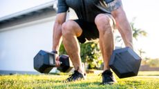 Man performing dumbbell squat on grass at home