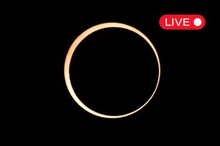 a ring of fire annular solar eclipse appearing as a golden yellow ring of light against a black background. in the top right corner there is a little graphic with "live" written in white text on a red background. 