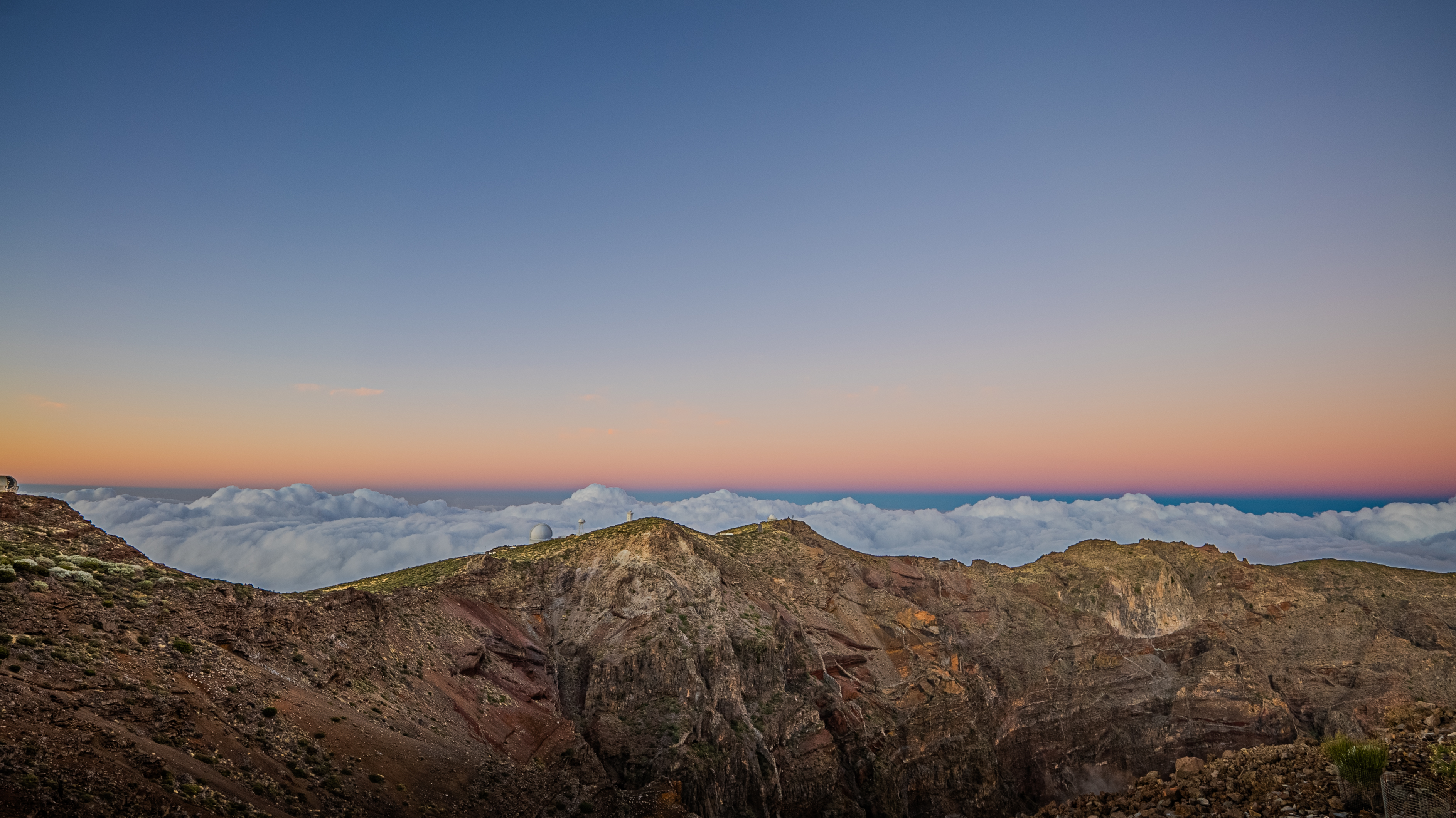 several white telescope domes on rock formations with pink and blue sky above.