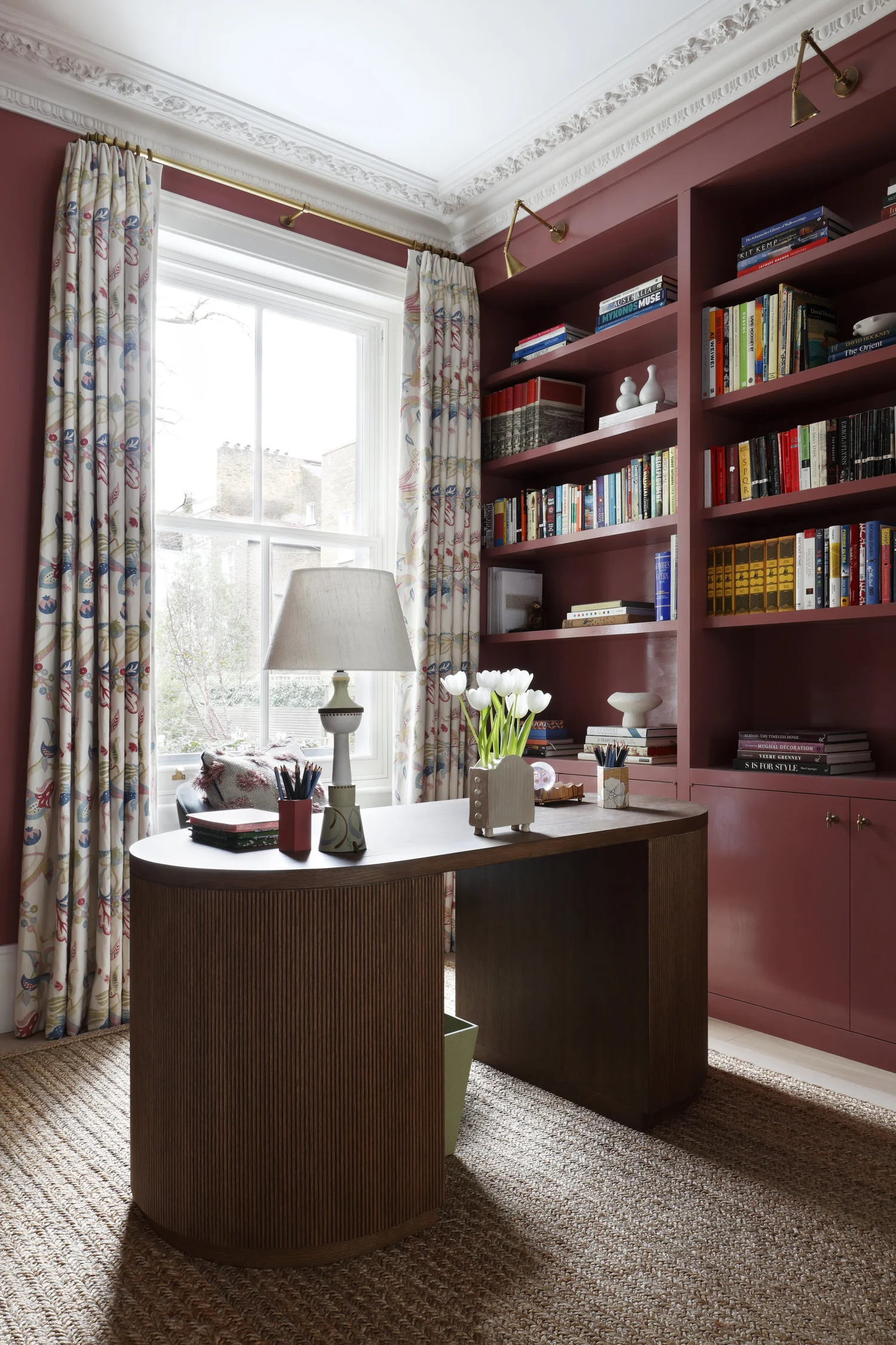 Red-painted study with woven jute rug, wooden desk and patterned curtains