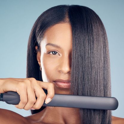 woman using a hair straightener to straightener her hair
