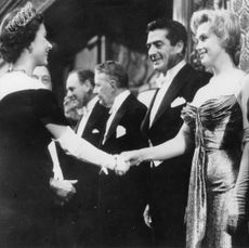 Queen Elizabeth wearing a tiara and evening gown shaking hands with Marilyn Monroe