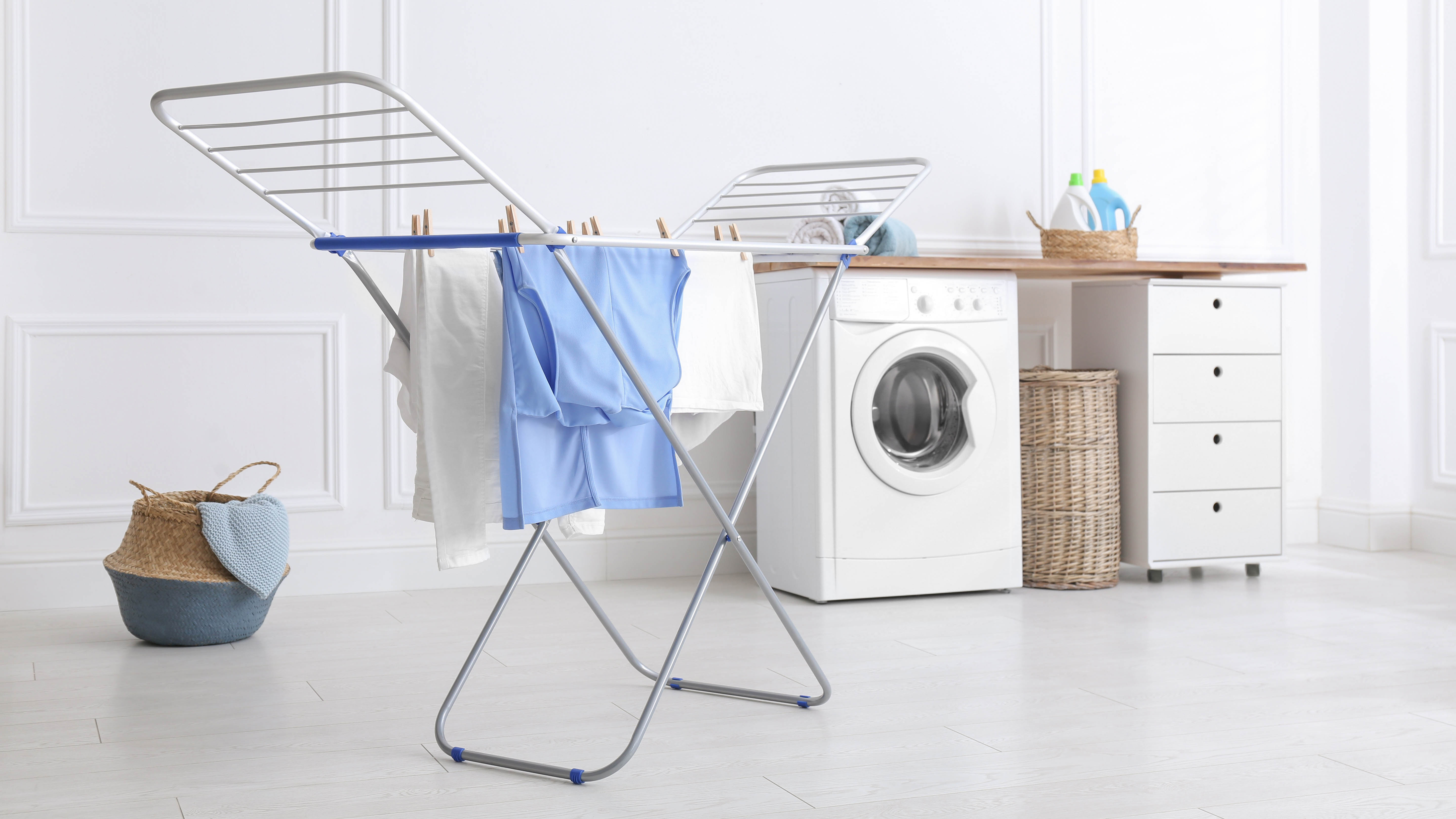 A drying rack drying clothes with a washing machine and laundry basket in the background