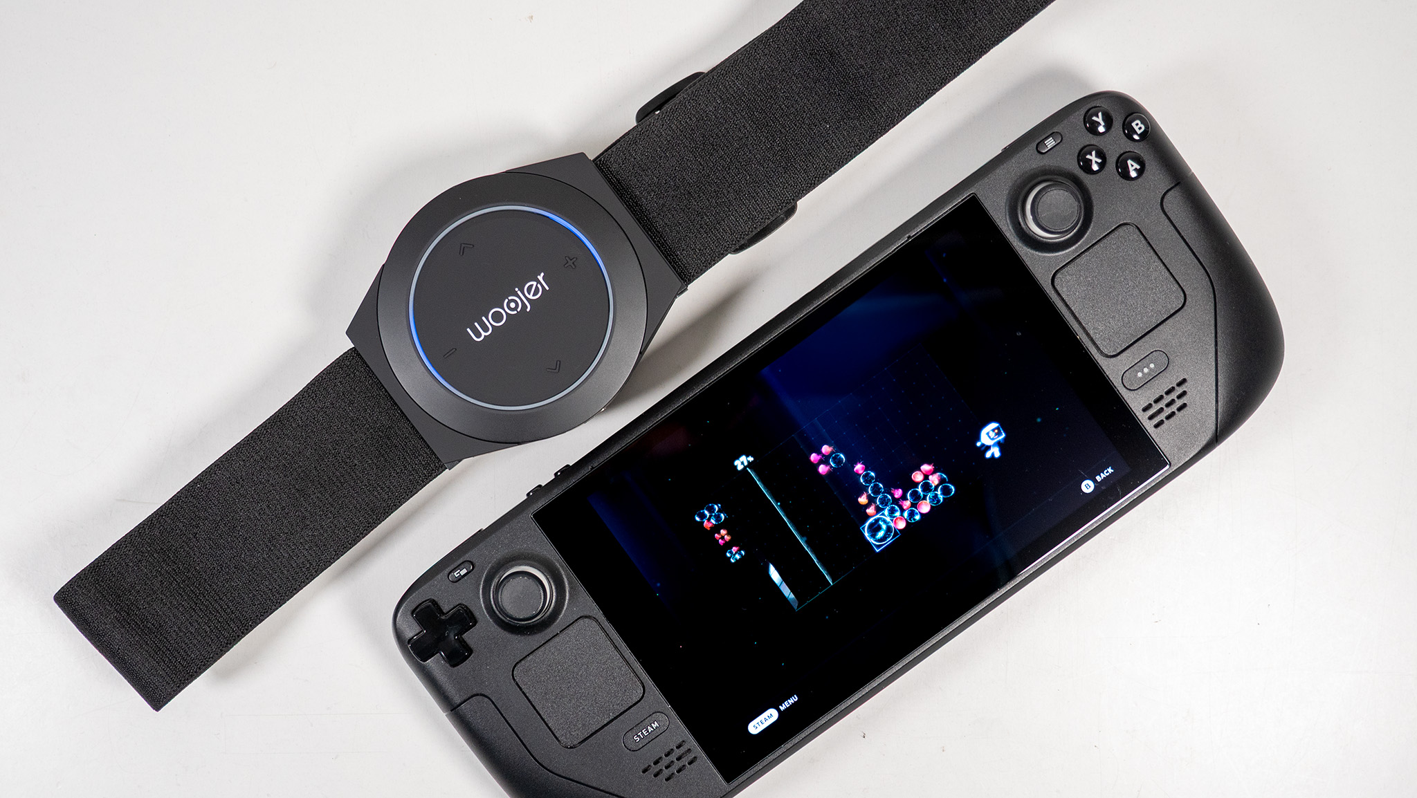 Ένα Woojer Body Strap 4 δίπλα σε ένα Steam Deck που παίζει το Lumines Arise