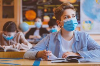 Middle school boy in mask looks up from classroom desk.