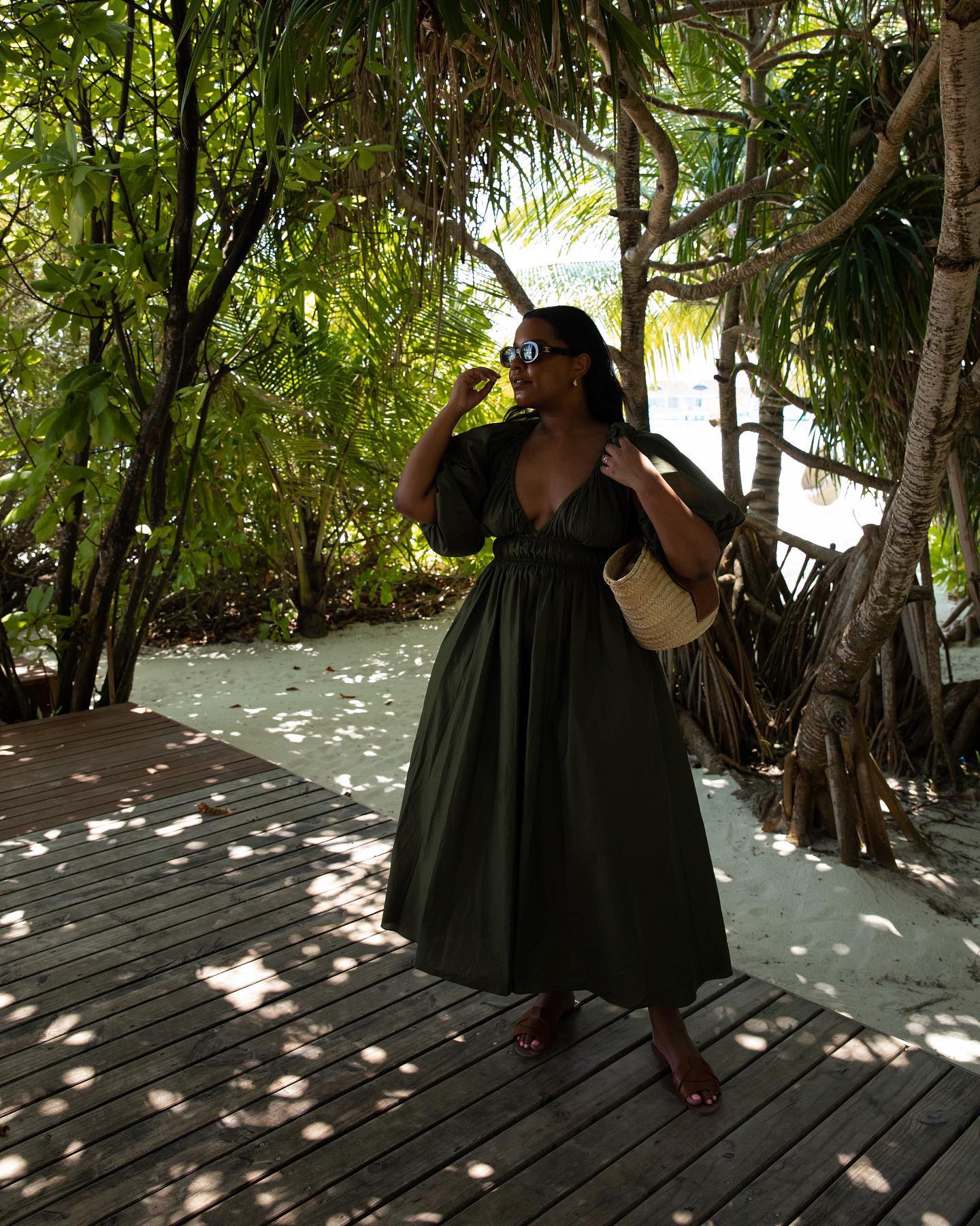 Woman on beach wears green dress, sandals and basket bag