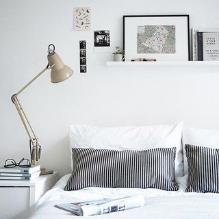 A bedroom with white walls furnished with a bed with white linen and a retro angle poise lamp on the bed side table.
