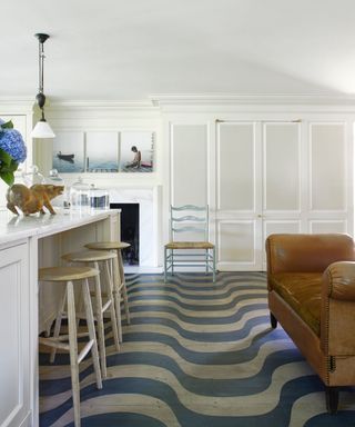 modern kitchen with white walls and white island, wood flooring with blue curved patter and tan brown sofa