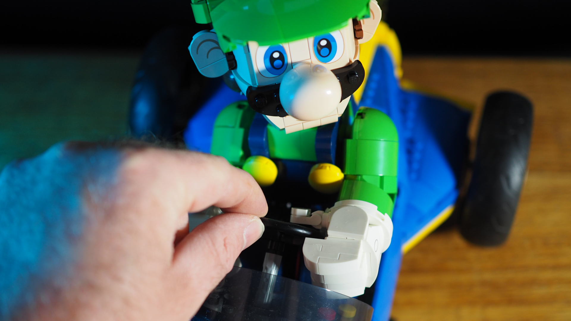 A hand reaches down to move the steering wheel of the Lego Luigi &amp;amp; Mach 8 set