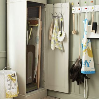 Neutral utility room, grey storage cupboard, storing vintage retro ironing board and cleaning accessories, hooks with various brushes, feather duster, dustpan and brush