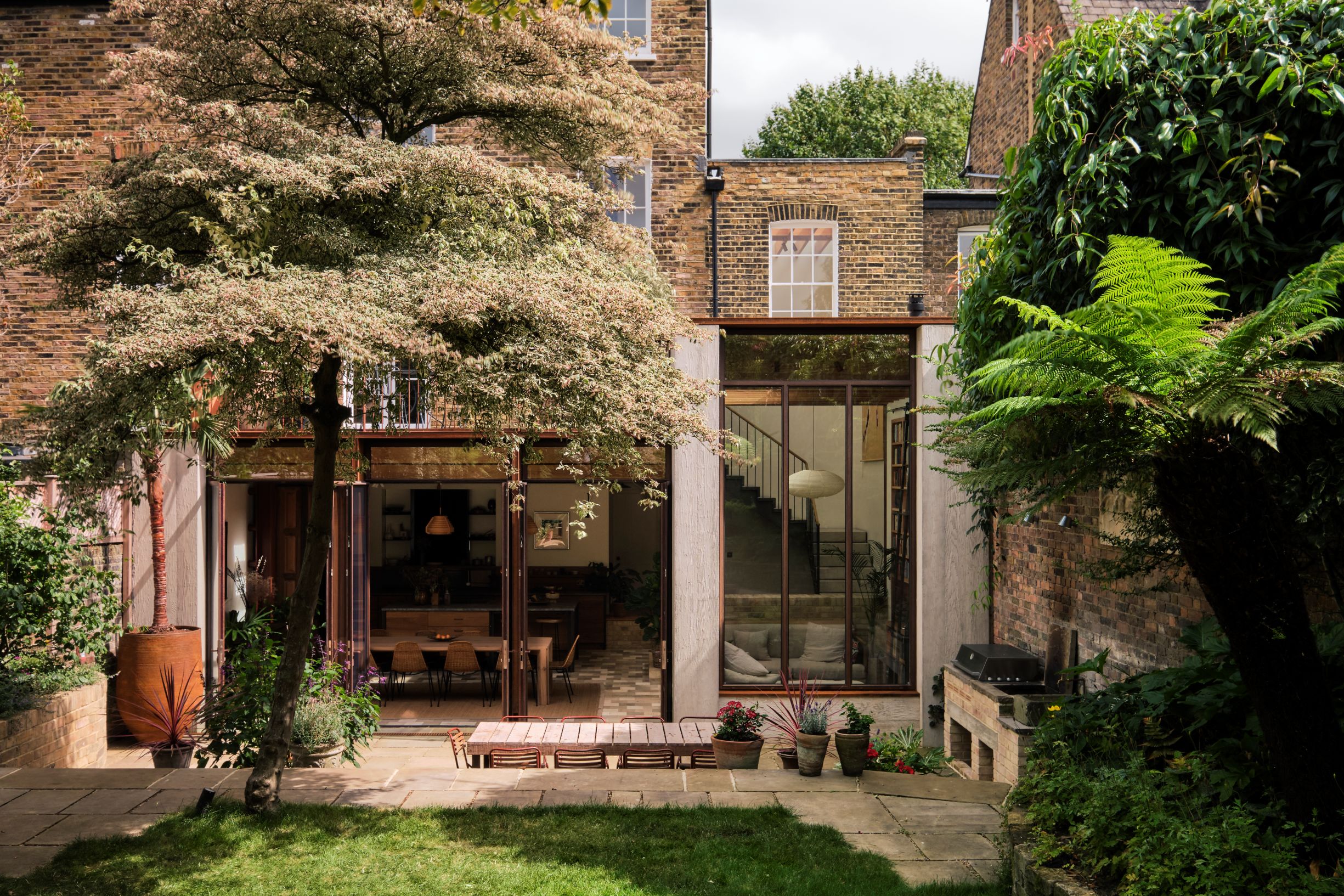modern extension on a victorian home, viewed from the split-level garden, with a paved sunken area and a grassy upper level