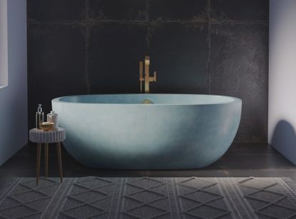 A blue concrete bath tub in a bathroom with a large rug and tiled wall