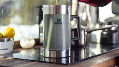Stanley Stay Hot French Press on a countertop with stainless steel pans and a Stanley fruit bowl in the background