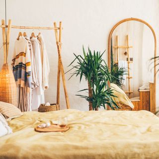 boho bedroom with mirror yellow comforter, a garment rack and plant