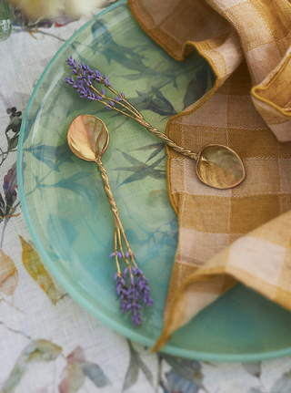 blue translucent plate with a floral tablecloth peeking underneath and teaspoons and checkered napkin placed on top