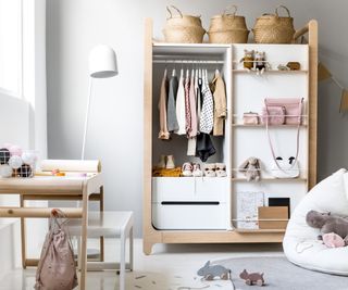 white and wooden wardrobe with children's clothes, a desk, chair and cream beanbag on floor