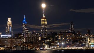 A lit up cityscape at night, with various tall towers looking over smaller industrial buildings, with a waterfront in front of the city.