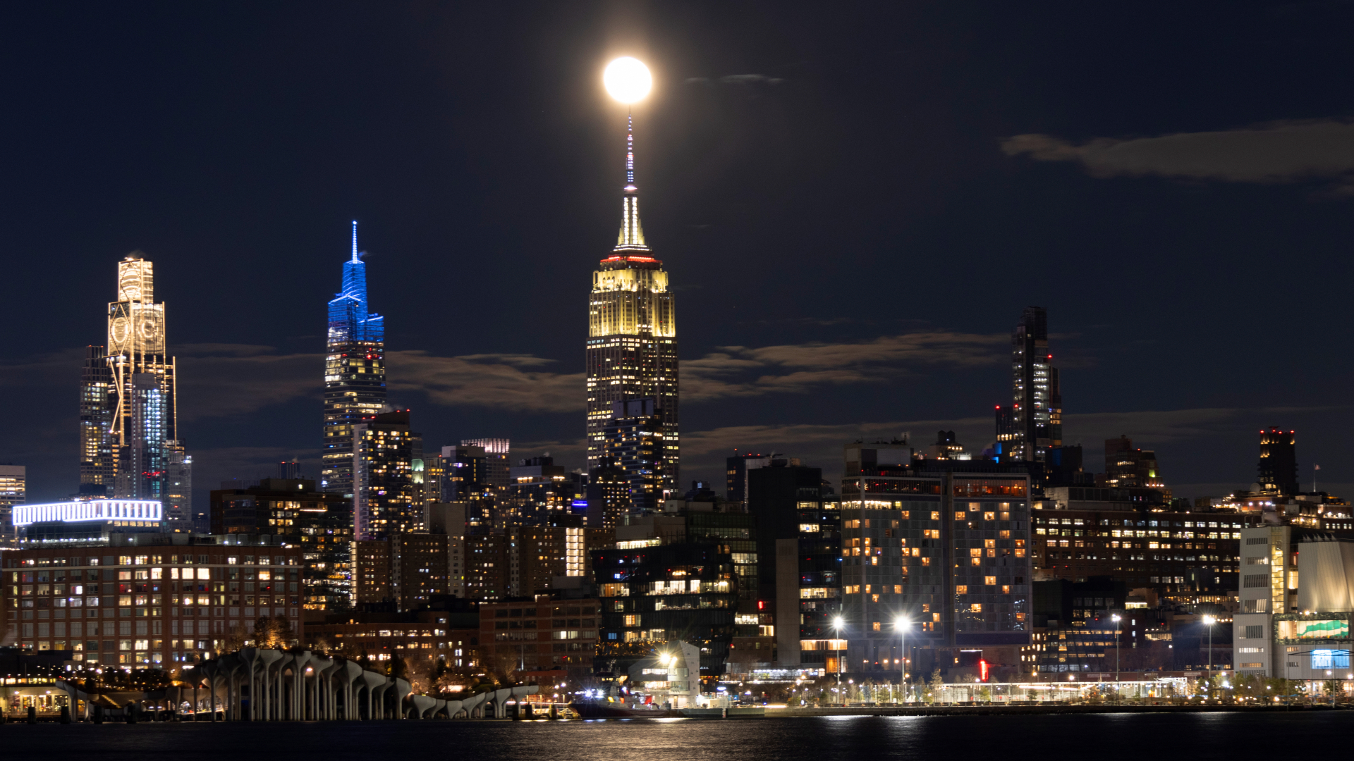 A lit up cityscape at night, with various tall towers looking over smaller industrial buildings, with a waterfront in front of the city.