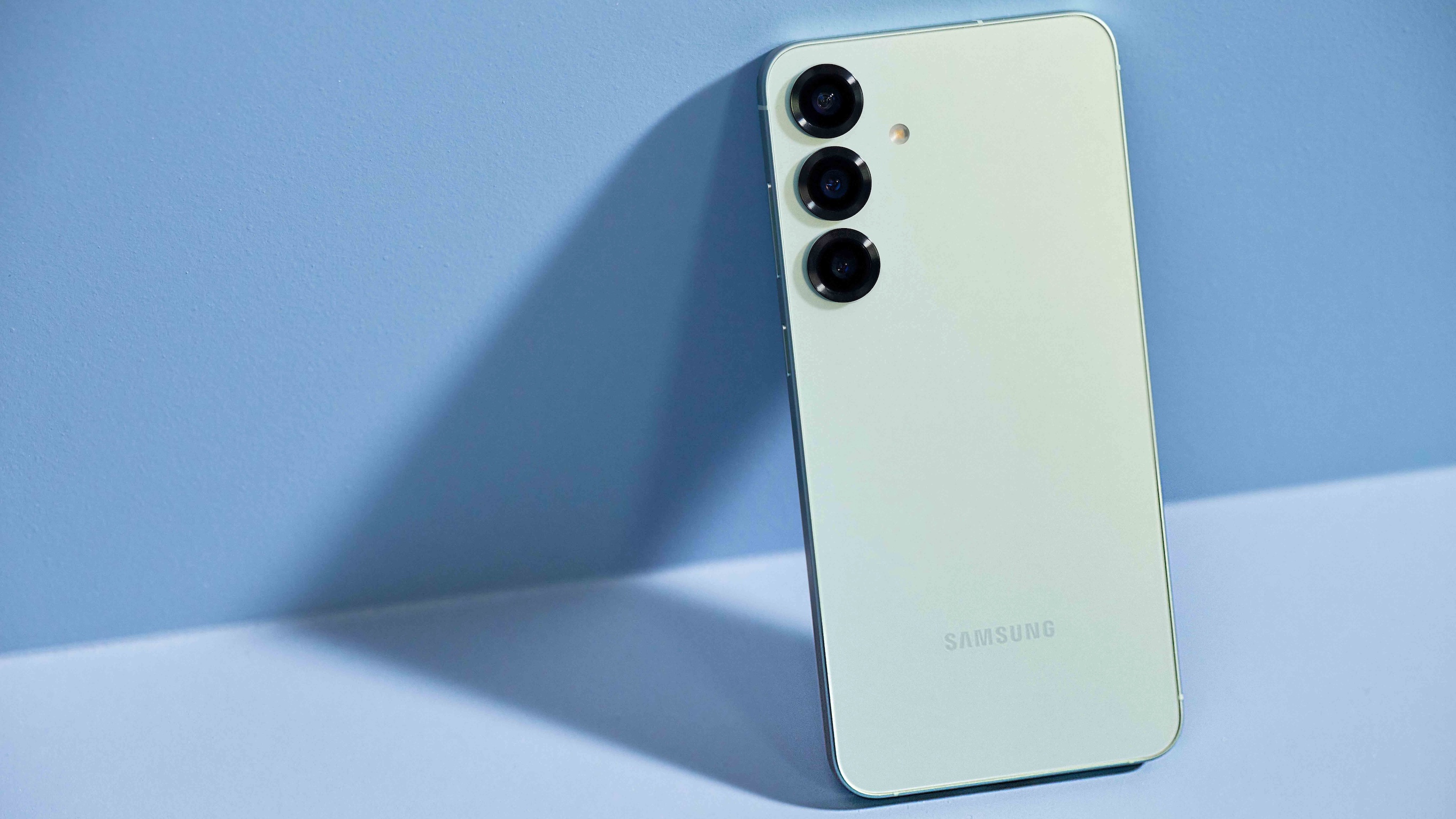 The Samsung Galaxy S25 seen from behind, leaning against a blue wall on a blue surface.
