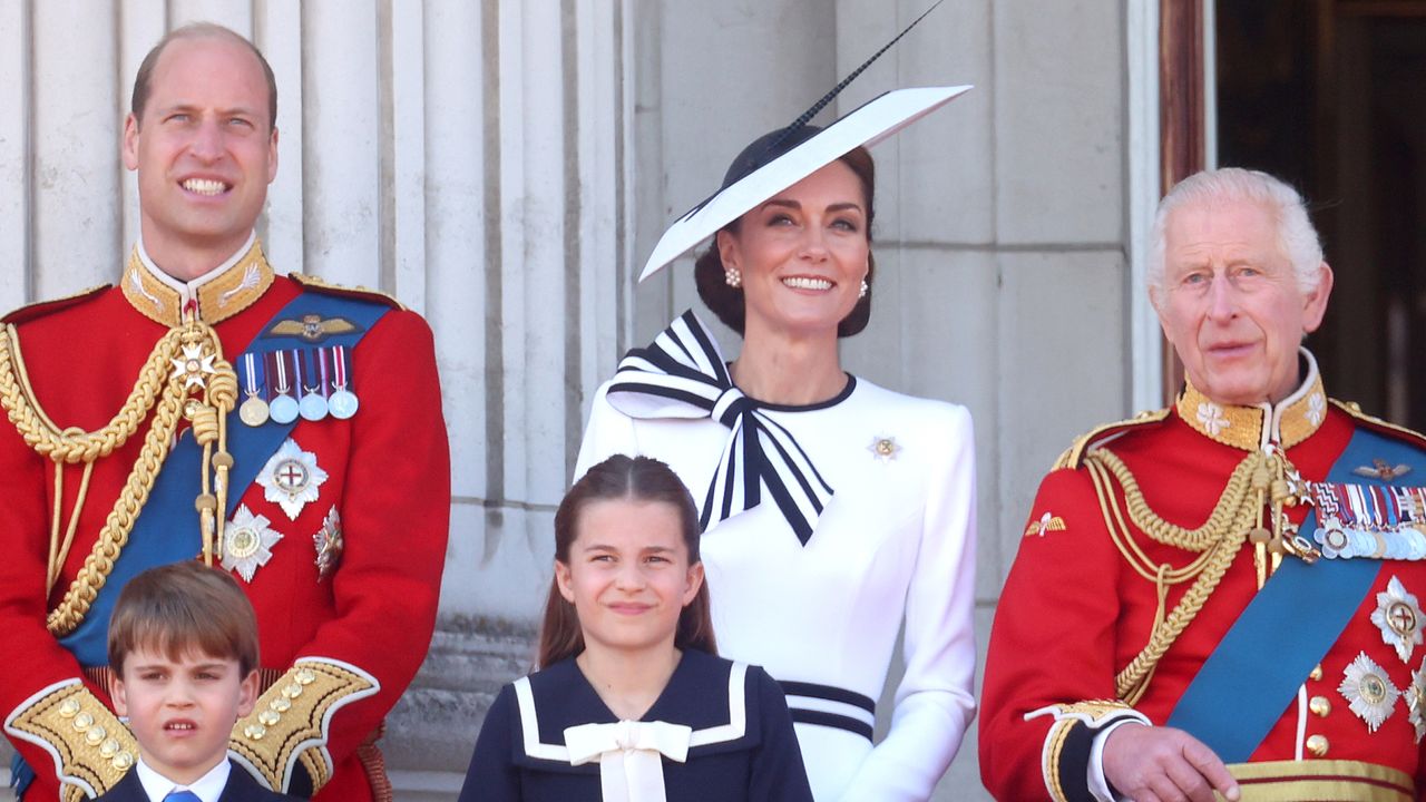 Kate Middleton wears a white dress with navy accents and a matching hat on the Buckingham Palace balcony with King Charles, who wears red military uniform