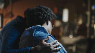 photo of two women sitting together, one with their arm around the other as if to comfort her