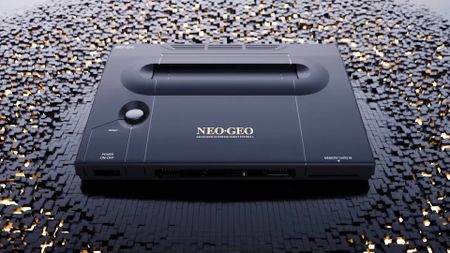 Neo Geo AES+ console in black sitting on fragmented surface made of black cubes.