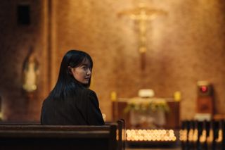 A woman (Shin Min-a) looks over her shoulder as she sits in a pew at a Catholic church, in 'Karma.'