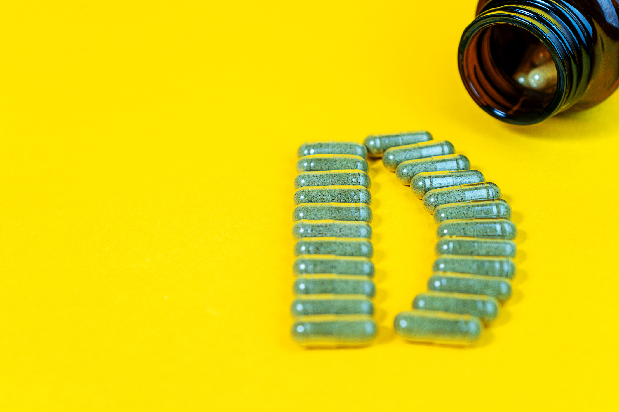 Yellow pills forming shape to D alphabet and vitamin D bottle on yellow background. Herbal nutritional supplements. Vitamin capsules, tablets. Alternative medicine and healthy concept.