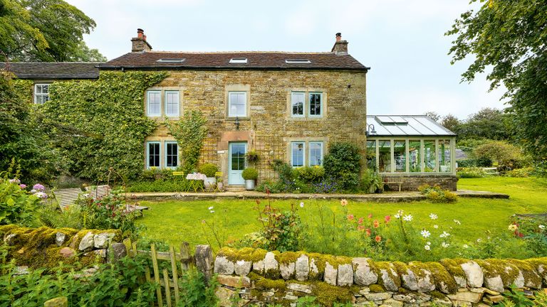 exterior of stone built farmhouse with conservatory and lawn in front