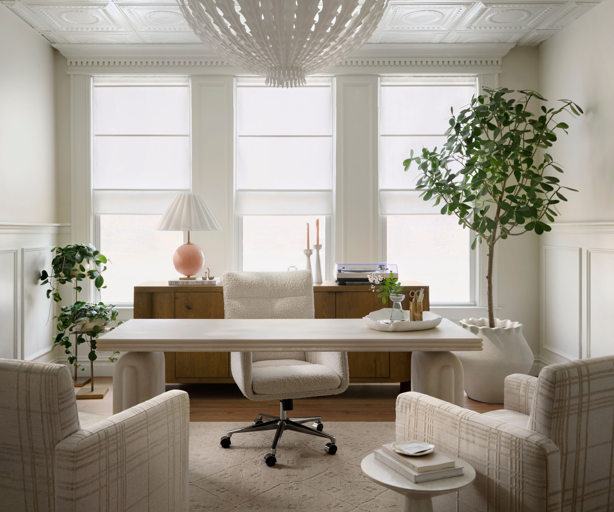 Office with moulded ceiling, desk with cream swivel chair, plaid armchairs and potted tree