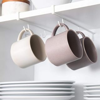 Inside of a kitchen cabinet with under-shelf hooks holding mugs