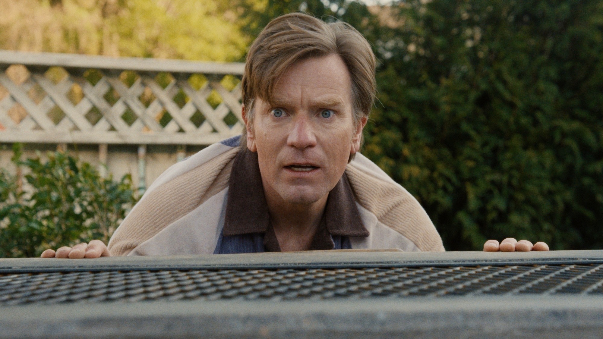 Ewan McGregor as Greg looking over a table in The End of Oak Street. 