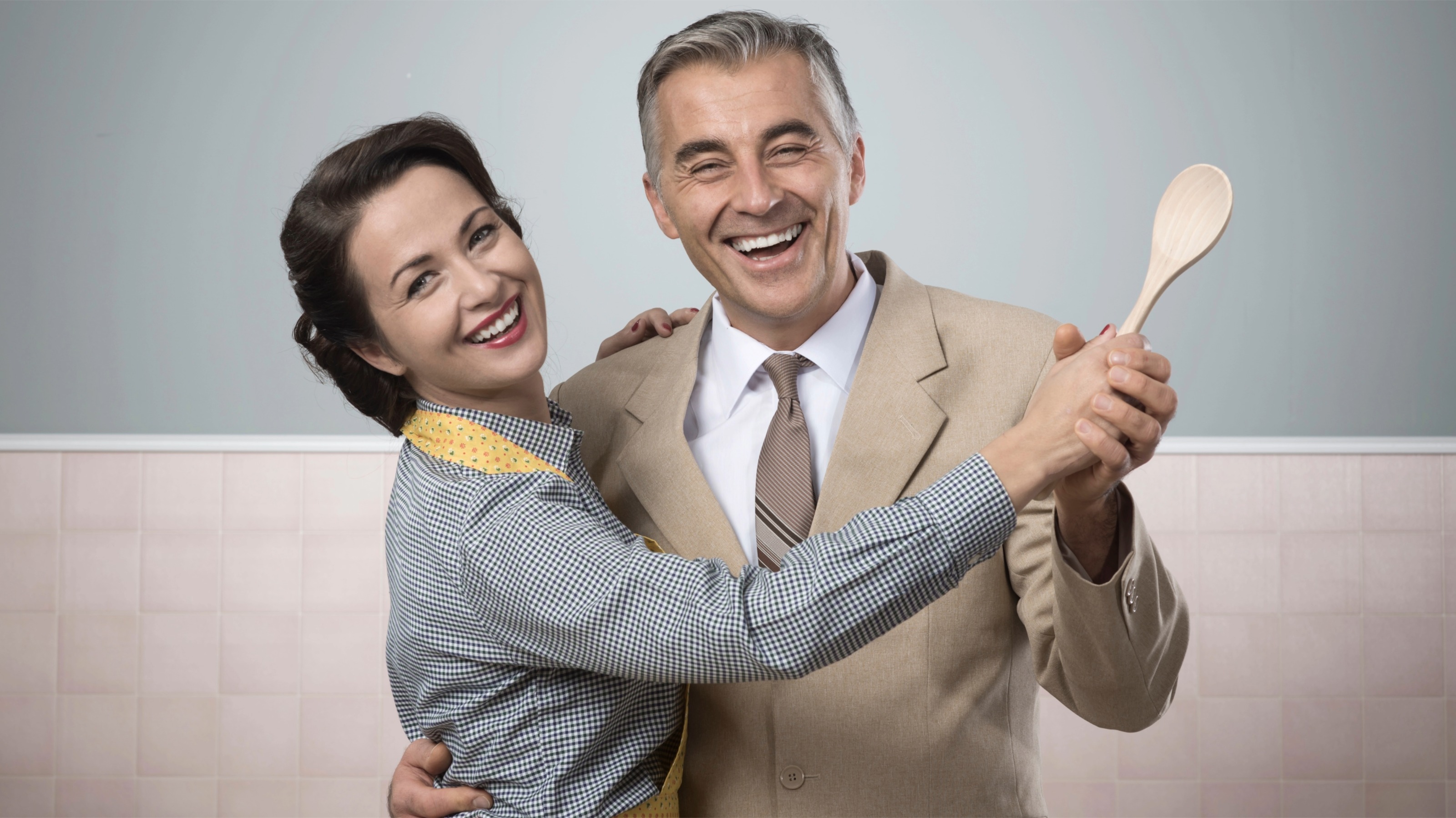 Smiling vintage couple dancing in the kitchen and holding a wooden spoon