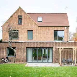 a view of the exterior of a three storey red brick house, with glass panel windows and a garden patio