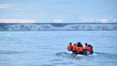 A small dinghy sails across the channel with a number of people on board wearing life jackets