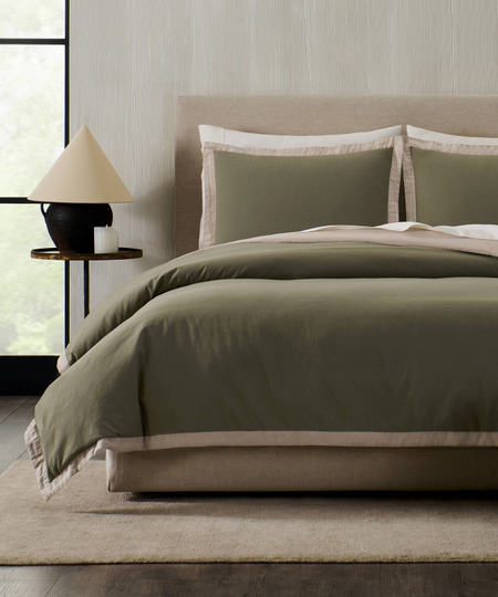 a bed made with green bedding and a small side table with a lamp on the left side