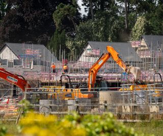 An orange digger in front of buildings with scaffolding around them