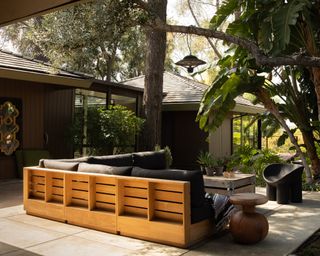 Patio space defined by wooden sectional and surrounded by large leafy palms and greenery