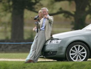 King Charles sitting on the bonnet of a blue car