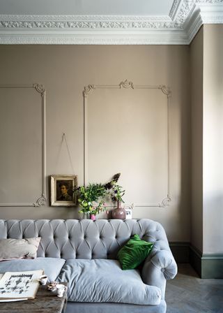 A beige living room with a gray velvet chesterfield sofa and a small framed painting behind it