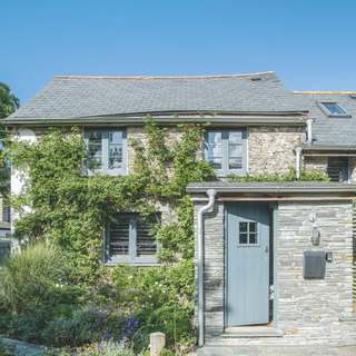 Front of the cottage with paved path, flower beds and blue front door. A renovated four bedroom Victorian house in Cornwall, home of Jill Stein.