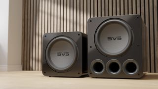 two SVS subwoofers on the floor against a wooden background wall.