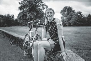 Josie Perry sentada en una pared sonriendo con su bicicleta al fondo