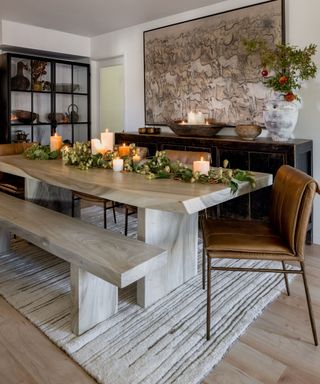 A rusting wooden dinign table with candles and a green foliage garland down the centre