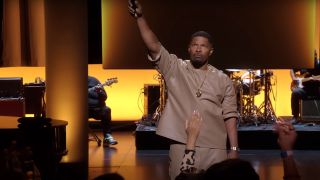 Jamie Foxx raising a microphone high on stage in Netflix's What Had Happened Was...