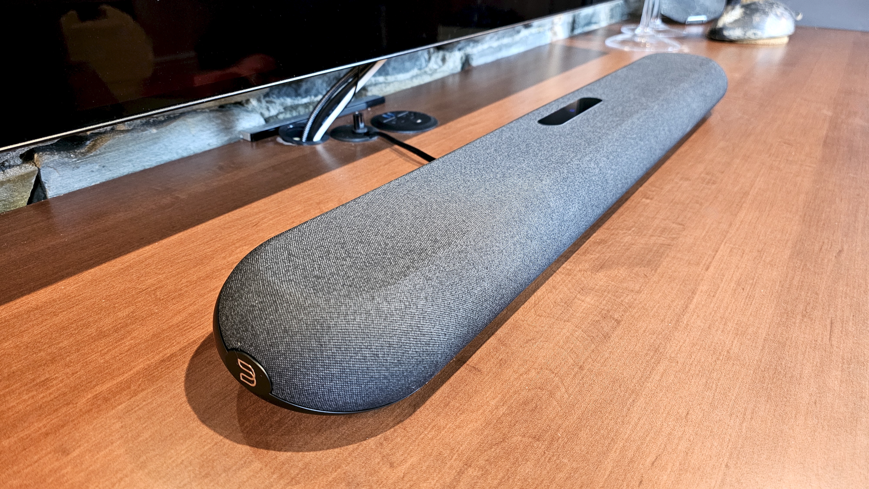 The Bluesound Pulse Mini soundbar pictured on a wooden cabinet under a TV